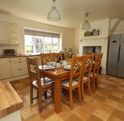 A kitchen with a wooden dining table set for six near a window and a stainless steel fridge at Rempstone Farmhouse Corfe Castle