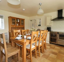 A kitchen with a wooden dining table and chairs set with dishes and food at Rempstone Farmhouse in Corfe Castle