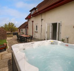 An outdoor patio area with a hot tub table and chairs near a beige building at Rempstone Farmhouse in Corfe Castle