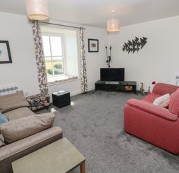 A living room with a beige sofa a red armchair a television on a black stand and a window with patterned curtains at Grassholm View in Solva