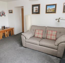 A living room with a grey sofa, a floor lamp, framed pictures on the wall, and nested wooden tables at Grassholm View in Solva