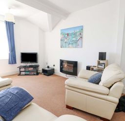 A living room with cream sofas a television and a wall-mounted electric fireplace at Bethan Apartment in Trearddur Bay