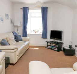 A living room with leather sofas a television on a stand and blue curtains at Bethan Apartment in Trearddur Bay