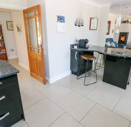 A kitchen with a granite countertop island and a stool and a living room with chairs and a fireplace at Llain Gwynfor in St Davids