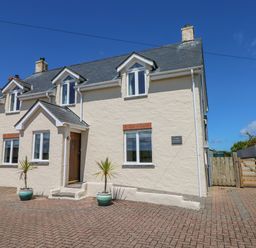 Exterior view of a two story cream house with a wooden front door and two potted plants on a brick driveway at Llain Gwynfor in St Davids
