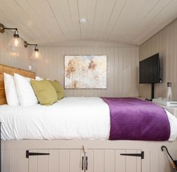 A bedroom with a wooden bed frame white bedding green pillows purple blanket wall art and a mounted television at Collen in Aberaeron