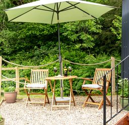 An outdoor seating area with two wooden chairs with cushions a small round table under a large umbrella and potted plants near a building at Bedwen in Aberaeron