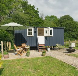 A small black shepherd hut with white windows and a door surrounded by gravel and outdoor furniture at Bedwen in Aberaeron