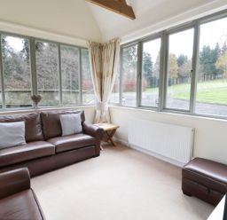 A living room with brown leather sofas and large windows overlooking a green lawn at The Folly in Belford