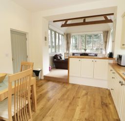 A kitchen with wooden floor and dining table next to a sitting area with sofas and large windows at The Folly in Belford