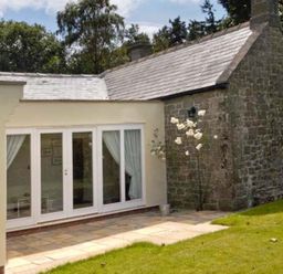 An exterior view of a house with a stone wall and glass doors opening to a patio with grass near Belford