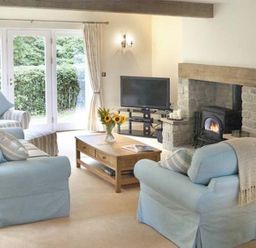 A living room with blue sofas a coffee table with flowers a fireplace and a television at The Lake Cottage Near Belford