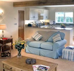 A living room with a blue sofa and striped ottoman next to a kitchen at The Lake Cottage Near Belford