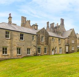 An exterior view of a large stone building with multiple chimneys and windows on a grassy slope at The Coach House in Belford