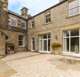 A stone courtyard with gravel and patio furniture outside a house with large windows at The Coach House in Belford