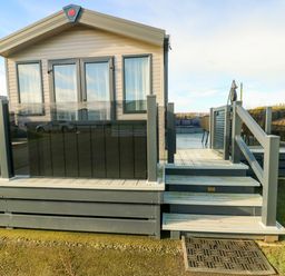 A small house with steps leading to a deck with glass railings and outdoor furniture at Cornerstone Near Caernarfon