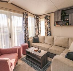 A living room with a beige sectional sofa a pink armchair two pink ottomans a coffee table and floral curtains at Cornerstone Near Caernarfon