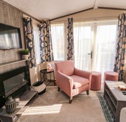 A living room with a pink armchair and ottomans a coffee table a wall-mounted TV and a fireplace at Cornerstone Near Caernarfon