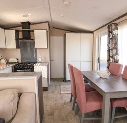 A kitchen and dining area with pink chairs around a wooden table and kitchen appliances at Cornerstone Near Caernarfon