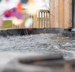 A bubbling hot tub outdoors next to a wooden deck railing at Cae Dafadd in New Mills near Llanfair Caereinion