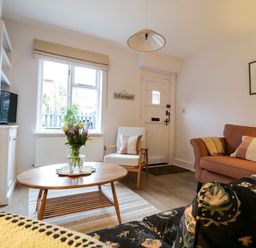 A living room with a wooden coffee table and flowers a sofa an armchair and a fireplace at Compass Cottage in Aldeburgh