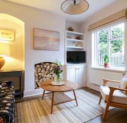A living room with a wooden coffee table and flowers on it a floral sofa and an armchair near a window at Compass Cottage in Aldeburgh