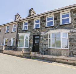 Two adjoining stone houses with bay windows and a black front door on a sloped street at Old Post Office in Blaenau Ffestiniog