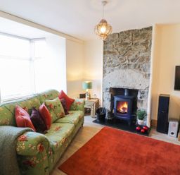 A living room with a floral sofa red pillows a stone fireplace with a stove and a red rug at Old Post Office in Blaenau Ffestiniog
