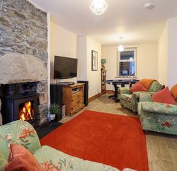 A living room with a stone fireplace wood stove television floral armchairs and a red rug at Old Post Office in Blaenau Ffestiniog