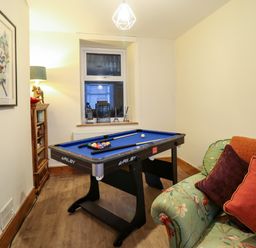 A room with a pool table a floral sofa with cushions a wooden cabinet and a window at Old Post Office in Blaenau Ffestiniog