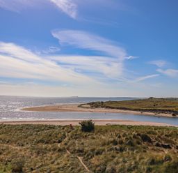 A coastal scene with grassy dunes a river flowing into the sea and a sandy beach at Ocean View in Alnmouth