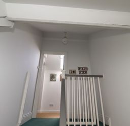 A hallway with white walls green carpet and a white stair railing at Ocean View in Alnmouth