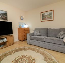 A living room with a grey sofa cushions a wooden chest of drawers and a television on a wooden stand at Archie's Minehead