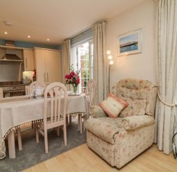 A dining area with a table set with a tablecloth and flowers next to a kitchen and a floral armchair at Archie's in Minehead