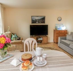 A living room with a dining table set with teapot and scones and a bouquet of flowers at Archie's in Minehead