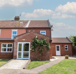 A brick house with multiple windows and doors a paved walkway and grass at Beach House in Winterton-On-Sea