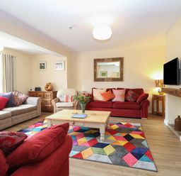 A living room with red and beige sofas a wooden coffee table and a colorful geometric rug at Beach House in Winterton-On-Sea