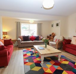 A living room with red sofas a wooden coffee table and a colorful geometric rug at Beach House in Winterton-On-Sea
