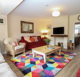 A living room with red sofas a wicker chair a wooden coffee table and a colorful geometric rug at Beach House in Winterton-On-Sea