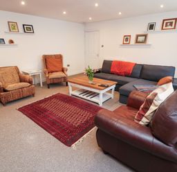 A living room with two wicker chairs a leather armchair a gray sofa a wooden coffee table and a red rug at The Old Factory House in Berwick-Upon-Tweed