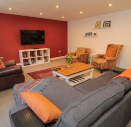 A living room with a gray sofa and orange pillows a wooden coffee table and a television on a red wall at The Old Factory House in Berwick-Upon-Tweed