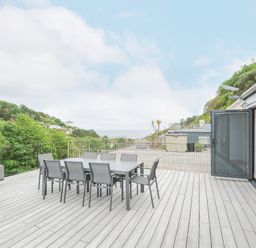 An outdoor terrace with a dining table and chairs a sofa and a coffee table overlooking trees and hills at 100 Hillside Villas in Looe