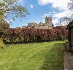 A garden with grass lawn and hedge with a stone castle behind at Snape Castle Garden Lodge Snape near Bedale
