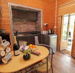 A kitchen with a table holding mugs a bottle a bowl of fruit and flowers at Snape Castle Garden Lodge in Snape near Bedale