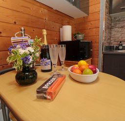 A kitchen table with a vase of flowers fruit bowl bottle of champagne and two glasses at Snape Castle Garden Lodge in Snape near Bedale