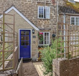 An exterior view of a stone cottage with a blue door and wooden trellis fencing at Old Ropemakers Cottage in Bridport