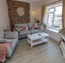 A living room with two gray sofas a white coffee table a TV on a stand and a window with a view at Fishnets in Brixham