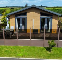 A wooden house with two glass doors opening onto a deck with a table and chairs at Lodge 18 - The Pines in Runswick Bay