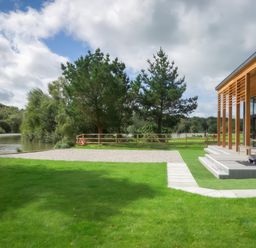 A lawn with a wooden modern building on the right and a lake with trees in the background at Silver Birch in Dolton