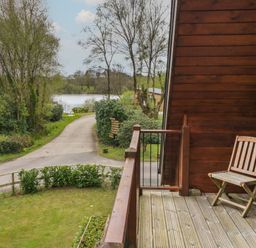 A wooden balcony with a chair overlooking a path and trees near a lake at Aspen in Dolton
